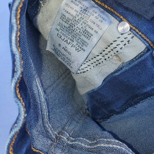 May include: A close-up of a blue denim jean label with white text. The label includes the text "RN 130273 CA 55384 MADE IN MEXICO OF US FABRIC HECHO EN MEXICO CON TELA DE RE.UU. FABRIQUE AU MEXIQUE DE TISSU EU. 78% COTTON / ALGODON 22% POLYESTER POLIESTER 2% BRANDEX ELASTANO 1910000268 73406 13JAFPW S REG".