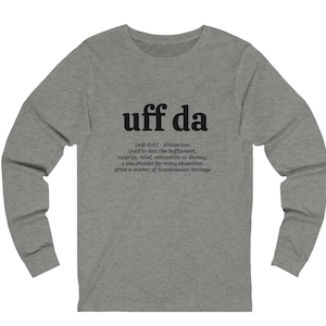 May include: Gray long-sleeve shirt with black text that reads "uff da [oof-duh] - interjection Used to describe bafflement, surprise, relief, exhaustion or dismay; a placeholder for many obsenities; often a marker of Scandinavian heritage"