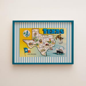 May include: A framed vintage map of Texas, featuring illustrations of landmarks and the state flag. The map is set against a striped background and framed in a teal blue border. The word "TEXAS" is prominently displayed.