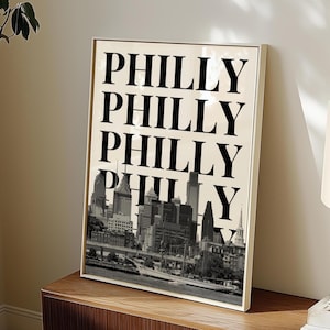 Könnte beinhalten: Ein gerahmter Druck mit einem Schwarzweißbild der Skyline von Philadelphia. Der Text "Philly" wird viermal in großen, fetten schwarzen Buchstaben wiederholt.