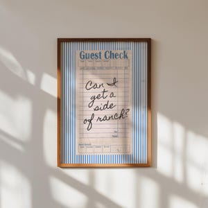 Könnte beinhalten: Gerahmter Druck eines Restaurantbelegs im Vintage-Stil mit blau-weiß gestreiftem Hintergrund. Der handgeschriebene Text lautet: „Can I get a side of ranch?“ Der Rahmen hat eine warme braune Farbe.