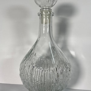 May include: A clear glass decanter with a textured, ribbed design. The decanter has a round, textured stopper.