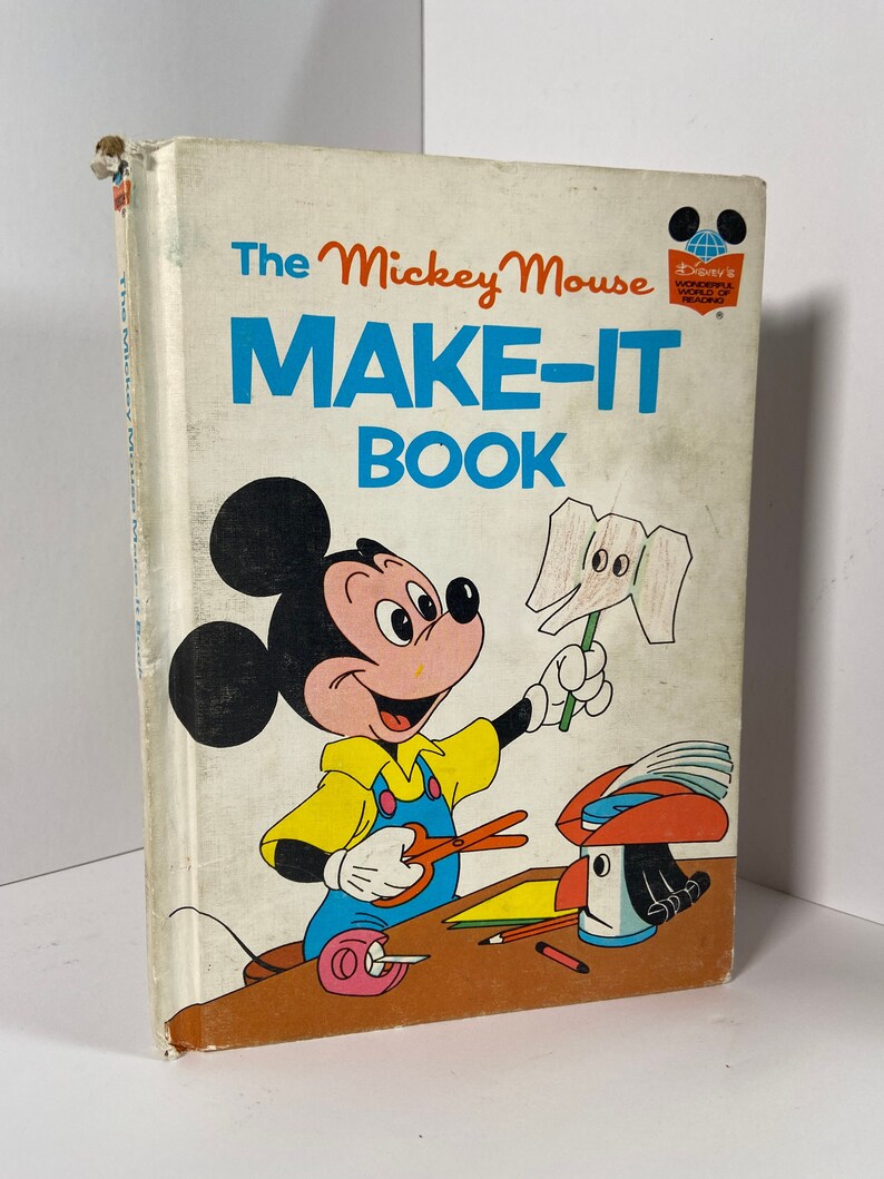 May include: A vintage children's book titled "The Mickey Mouse Make-It Book" featuring a cartoon illustration of Mickey Mouse making a craft project. The book cover is white with a red and blue Disney World of Reading logo.