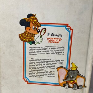 May include: A book cover featuring Mickey Mouse and Dumbo from Disney's Wonderful World of Reading series. The cover is red, white, and blue with a yellow and brown illustration of Mickey Mouse wearing a detective hat and holding a magnifying glass. Dumbo is sitting on the bottom right corner of the cover.