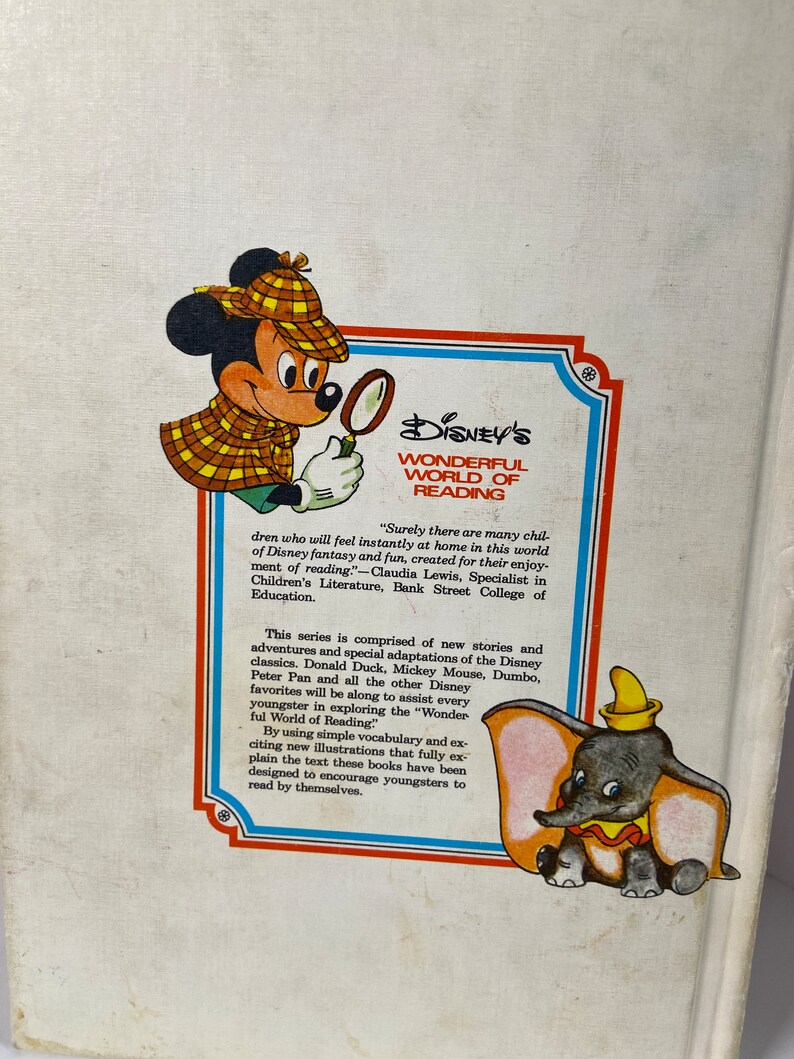 May include: A book cover featuring Mickey Mouse and Dumbo from Disney's Wonderful World of Reading series. The cover is red, white, and blue with a yellow and brown illustration of Mickey Mouse wearing a detective hat and holding a magnifying glass. Dumbo is sitting on the bottom right corner of the cover.