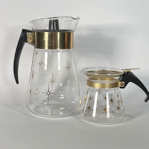 May include: Two glass coffee pots with gold star designs and black handles. The larger pot has a gold band around the top.