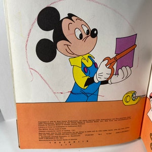 May include: Mickey Mouse is cutting out a purple piece of paper with a pair of orange scissors. The book cover features the text "The Mickey Mouse Make-It Book" and "Disney's Wonderful World of Reading".