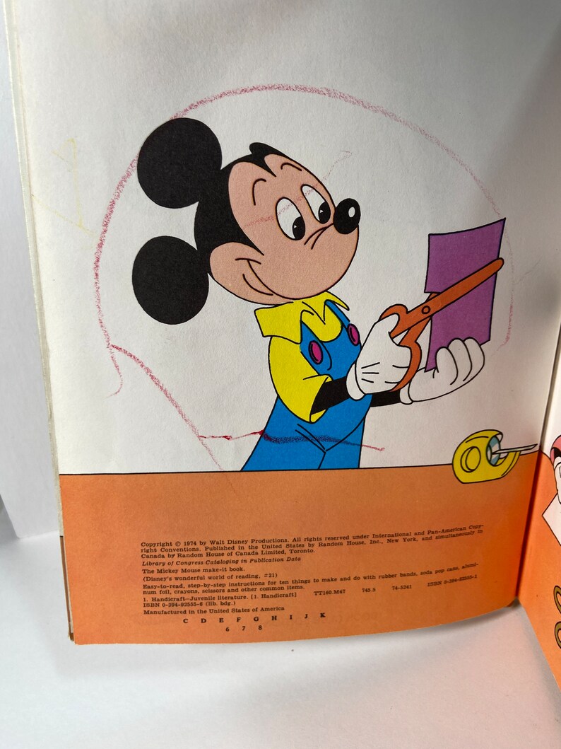 May include: Mickey Mouse is cutting out a purple piece of paper with a pair of orange scissors. The book cover features the text "The Mickey Mouse Make-It Book" and "Disney's Wonderful World of Reading".