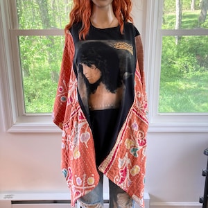 May include: A black t-shirt featuring a portrait of a musician, worn under a patterned orange and white jacket. The jacket has a floral design. The outfit is paired with ripped blue jeans.