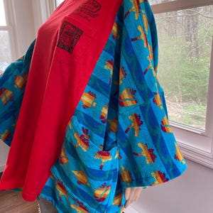 Pu&ograve; includere: Una maglietta rossa a maniche lunghe con tasca e maniche blu a righe e disegni tropicali. La maglietta ha una vestibilit&agrave; ampia e uno stile unico. Le maniche sono in tessuto fantasia.