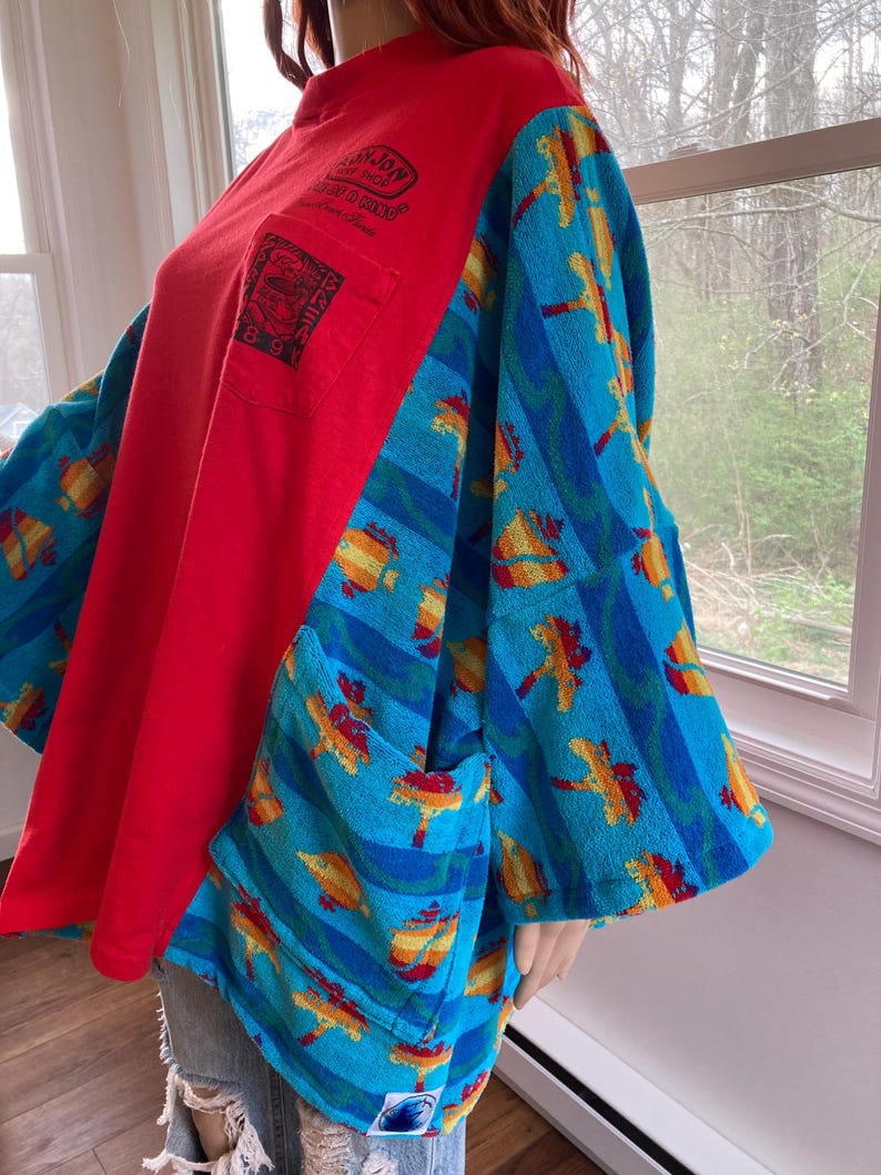 Pu&ograve; includere: Una maglietta rossa a maniche lunghe con tasca e maniche blu a righe e disegni tropicali. La maglietta ha una vestibilit&agrave; ampia e uno stile unico. Le maniche sono in tessuto fantasia.