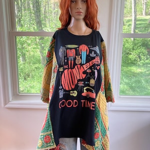 Può includere: Top nero stile tunica con una grafica dei Monkees e le parole "Good Time". Le maniche sono patchwork con motivi floreali rossi, verdi e gialli. Il manichino indossa jeans blu strappati.