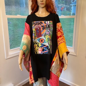 May include: A black tunic featuring a Star Trek comic book graphic on the front, with wide, multicolored patchwork sleeves and side panels in shades of red, orange, yellow, and green, worn over light blue distressed denim jeans.
