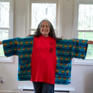 Pu&ograve; includere: Una maglietta rossa con una piccola grafica sulla tasca &egrave; indossata sotto un kimono a fantasia turchese e giallo. Il kimono presenta un motivo ripetuto di forme gialle e arancioni su sfondo turchese. La persona indossa jeans blu.