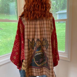 May include: A patchwork kimono-style jacket with a Def Leppard graphic on the back. The jacket features a plaid pattern, red floral sleeves, and denim accents. The Def Leppard graphic is in a triangle shape with a mouth and the words "Love Bites".