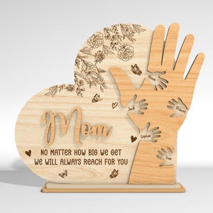 May include: Wooden heart-shaped sign with the word "Mom" and a message that reads "No matter how big we get we will always reach for you". The heart is surrounded by five handprints with names written on each hand.