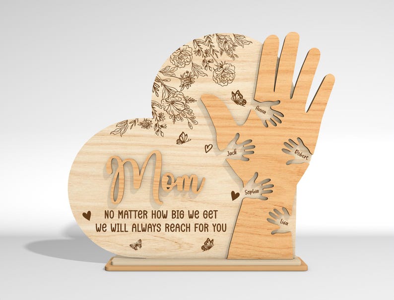 May include: Wooden heart-shaped sign with the word "Mom" and a message that reads "No matter how big we get we will always reach for you". The heart is surrounded by five handprints with names written on each hand.