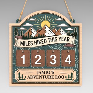Könnte beinhalten: Holzschild mit Berg- und Sonnendesign, mit der Aufschrift "Miles Hiked This Year" und "Jamio's Adventure Log". Verfügt über vier Zahlenkacheln zur Verfolgung. Enthält eine Aufhängeschnur.