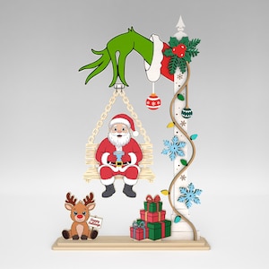 May include: A whimsical Christmas decoration featuring Santa Claus on a swing, a reindeer holding a sign, and a stack of presents. The Grinch's green hand reaches down from above. The design includes snowflakes and decorative lights.
