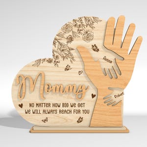 May include: Wooden heart-shaped sign with the word "Mommy" and the text "No matter how big we get we will always reach for you". Two handprints are on the sign with the names "Anna" and "Robert" written below them.