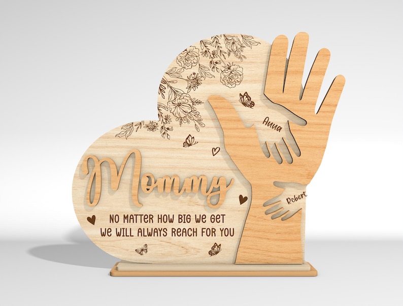 May include: Wooden heart-shaped sign with the word "Mommy" and the text "No matter how big we get we will always reach for you". Two handprints are on the sign with the names "Anna" and "Robert" written below them.