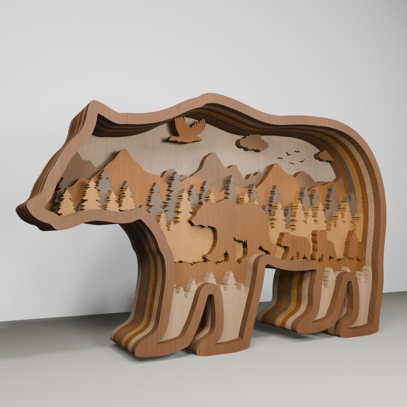 K&ouml;nnte beinhalten: Eine Holz-B&auml;rensilhouette mit einem geschichteten Design. Das Innere des B&auml;ren ist ausgeschnitten, um eine Waldszene mit Bergen, B&auml;umen und einer B&auml;renfamilie zu zeigen.