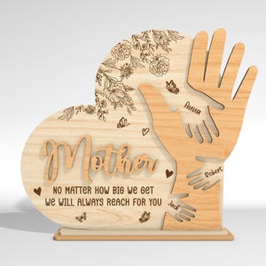 May include: Wooden heart-shaped plaque with the word "Mother" and the text "No matter how big we get we will always reach for you". Three handprints are engraved on the plaque with the names "Anna", "Robert", and "Jack" written below each handprint.