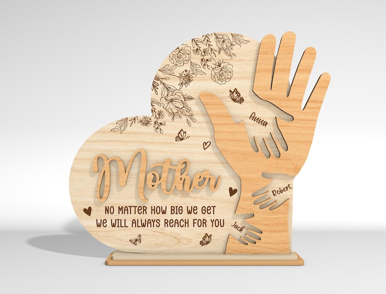May include: Wooden heart-shaped plaque with the word "Mother" and the text "No matter how big we get we will always reach for you". Three handprints are engraved on the plaque with the names "Anna", "Robert", and "Jack" written below each handprint.