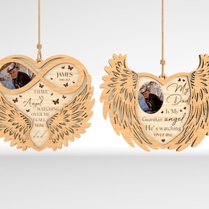 Op de afbeelding: Twee houten ornamenten in de vorm van een hart met vleugels. De ornamenten hebben een fotolijst in het midden. De tekst op de ornamenten luidt "Ik heb een engel die over me waakt, ik noem hem papa" en "Mijn vader is mijn beschermengel, hij waakt over me".