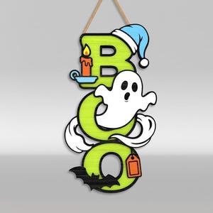 Op de afbeelding: Een verticaal hangbord met de tekst BOO in limoengroene letters. De B heeft een blauwe slaapmuts en een brandende oranje kaars. Een wit spook zweeft door de O en een zwarte vleermuis is aan de onderkant van de laatste O bevestigd met een oranje label.