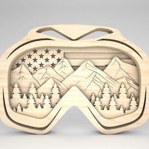 May include: Wooden cutout of a pair of ski goggles with a mountain scene and an American flag inside the lens.
