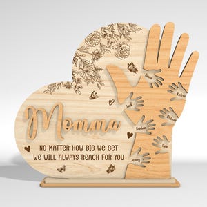 May include: Wooden heart-shaped sign with the word "Momma" and the text "No matter how big we get we will always reach for you". The heart is surrounded by handprints with names written on each handprint.