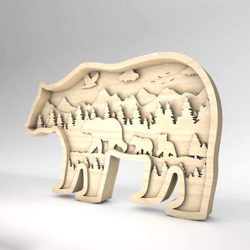 K&ouml;nnte beinhalten: Eine Holz-B&auml;rensilhouette mit einem Ausschnitt-Design einer Waldszene, einschlie&szlig;lich Bergen, B&auml;umen und einer B&auml;renfamilie. Der B&auml;r steht auf einer grasbewachsenen Wiese mit einem blauen Himmel dar&uuml;ber.