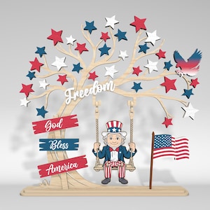 May include: Wooden patriotic decoration featuring a tree adorned with red, white, and blue stars. The word "Freedom" is displayed, along with Uncle Sam on a swing, an American flag, and the words "God Bless America."