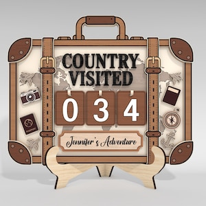 May include: Wooden travel-themed sign in the shape of a suitcase. The sign reads "COUNTRY VISITED" and displays the number "034". Includes a world map, passport, camera, and compass. The sign also has the text "Jennifer's Adventure".
