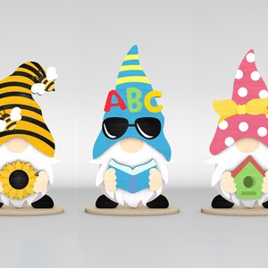 May include: Three wooden gnome figurines. One gnome wears a yellow and black striped hat with a bee and holds a sunflower. Another gnome has a blue hat with the letters ABC and sunglasses, holding a book. The third gnome wears a pink polka-dot hat and holds a birdhouse.