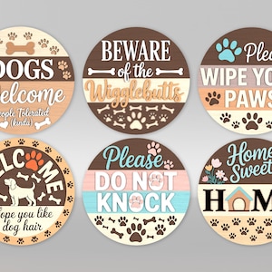 Puede incluir: Una colección de seis letreros redondos de madera con frases temáticas de perros. Los letreros presentan huellas de patas, huesos y frases como "Dogs Welcome" y "Home Sweet Home". Los colores incluyen marrón, beige y varios tonos pastel.