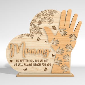 May include: Wooden heart-shaped sign with the word "Mommy" and the text "No matter how big we get we will always reach for you". The heart is surrounded by a design of hands with names written on each hand.