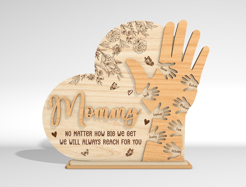 May include: Wooden heart-shaped sign with the word "Mommy" and the text "No matter how big we get we will always reach for you". The heart is surrounded by a design of hands with names written on each hand.