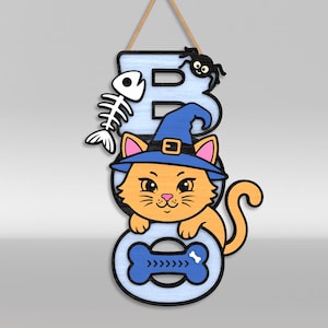 Op de afbeelding: Een hangend wandbord met de tekst BOO in lichtblauwe letters. De letter B is voorzien van een wit vissenskelet en een zwarte spin. Een oranje kat met een blauwe heksenhoed zit in het midden en de letter O bevat een blauwe botvorm.