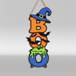 Op de afbeelding: Een verticaal hangend wandbord met de tekst BOO. De letter B is oranje met een blauwe heksenhoed. De letter O is oranje met zwarte vleermuissilhouetten. De laatste O is een blauwe ketel met groene borrelende vloeistof, opgehangen aan een touw.