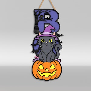 Op de afbeelding: Een hangend houten bord met de letter B in paars met een zwart boomsilhouet en een kleine kat. Een grijze kat met een paarse heksenhoed zit op een oranje pompoen met gele ogen en mond, omringd door kleine snoepjes.