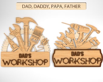 May include: Wooden sign with the text "Dad's Workshop" in brown lettering. The sign is decorated with a variety of tools, including a hammer, wrench, screwdriver, and saw. The tools are cut out of the wood and are arranged in a circular pattern.