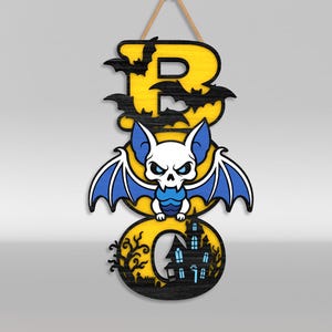 Op de afbeelding: Een verticaal hangend bord met het woord BOO in gele letters met zwarte omlijning. De letter B is versierd met zwarte vleermuissilhouetten. Een wit en blauw vleermuisfiguur zit tussen de letters. De letter O bevat een afbeelding van een zwart spookhuis.