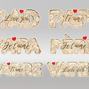 Op de afbeelding: Een set van acht houten uitsnijdingen met verschillende woorden voor vader in verschillende talen. De woorden zijn "DAD", "PAPI", "PAPA", "PÈRE", "PADRE", "VATER", en elk woord is omgeven door een ontwerp van gereedschap. Elke uitsnijding heeft een klein rood hart boven het woord.