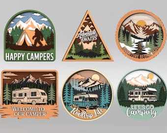 May include: A collection of six layered wooden camping-themed signs. Designs include a tent with a Bigfoot, a mountain scene with the text "Adventure Begins Here", a camper with the text "Welcome to Our Camper", and other camping-related phrases.