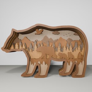 K&ouml;nnte beinhalten: Eine Holz-B&auml;rensilhouette mit einem geschichteten Design. Das Innere des B&auml;ren ist ausgeschnitten, um eine Waldszene mit Bergen, B&auml;umen und einer B&auml;renfamilie zu zeigen.
