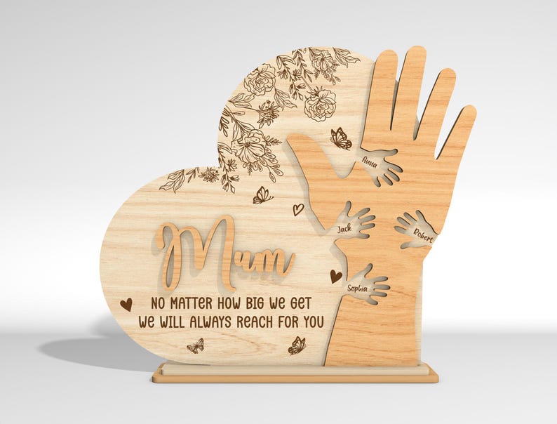 May include: Wooden heart-shaped plaque with the word "Mum" and a message that reads "No matter how big we get we will always reach for you". The plaque features a design of hands reaching up towards the word "Mum" with names inscribed on each hand.