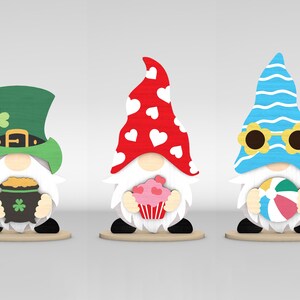May include: Three wooden gnome figurines. One wears a green hat with a shamrock and holds a pot of gold. Another has a red hat with white hearts and holds a cupcake. The last gnome wears a blue hat with sunglasses and holds a beach ball.