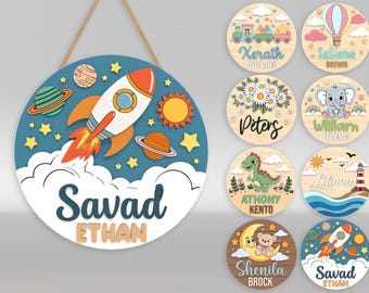 May include: A round wooden sign with a space theme, featuring a rocket ship, planets, stars, and the names "Savad" and "Ethan". Additional signs with various designs, including a train, hot air balloon, flowers, elephant, dinosaur, lighthouse, moon, and rocket ship.